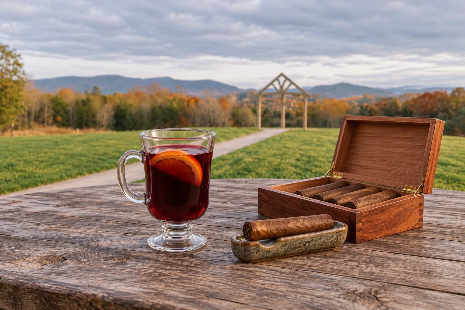 Cigars in a cedar box and on a separate rest beside mulled wine, with an Ayoka Ranch-inspired landscape